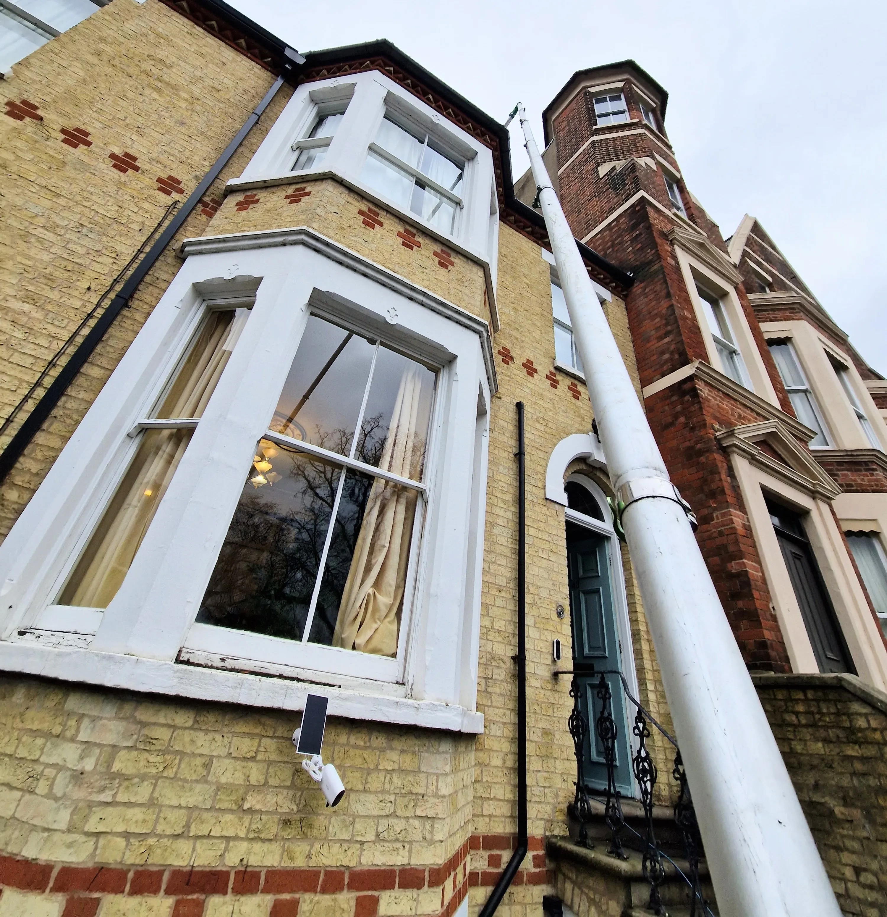 A gutter vacuum pole reaching up to the gutter of a three-storey Victorian terraced house in Cambridge.
